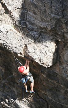 A rock climber works his way up a rock face protected by a rope clipped into bolts. He is wearing a helmet and quickdraws dangle from his harness. The route is in the desert southwest United States. Mt Lemmon, Arizona.