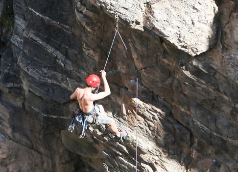 A rock climber works his way up a rock face protected by a rope clipped into bolts. He is wearing a helmet and quickdraws dangle from his harness. The route is in the desert southwest United States. Mt Lemmon, Arizona.