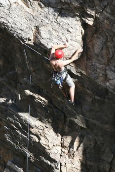 A rock climber works his way up a rock face protected by a rope clipped into bolts. He is wearing a helmet and quickdraws dangle from his harness. The route is in the desert southwest United States. Mt Lemmon, Arizona.