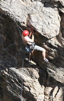 A rock climber works his way up a rock face protected by a rope clipped into bolts. He is wearing a helmet and quickdraws dangle from his harness. The route is in the desert southwest United States. Mt Lemmon, Arizona.