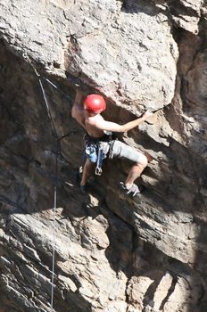 A rock climber works his way up a rock face protected by a rope clipped into bolts. He is wearing a helmet and quickdraws dangle from his harness. The route is in the desert southwest United States. Mt Lemmon, Arizona.