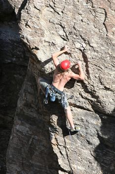 A rock climber works his way up a rock face protected by a rope clipped into bolts. He is wearing a helmet and quickdraws dangle from his harness. The route is in the desert southwest United States. Mt Lemmon, Arizona.