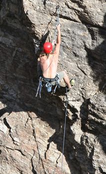 A rock climber works his way up a rock face protected by a rope clipped into bolts. He is wearing a helmet and quickdraws dangle from his harness. The route is in the desert southwest United States. Mt Lemmon, Arizona.