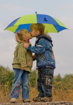 Little boy kiss girl, under umbrella in autumn day