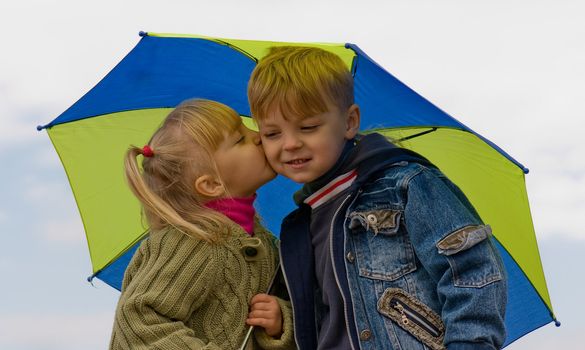 Little girl kiss boy, under umbrella in autumn day