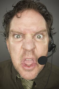 Irate Businessman Wearing a Phone Headset Against a Grey Background.