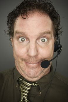 Giddy Businessman Smiles Wearing a Phone Headset Against a Grey Background.