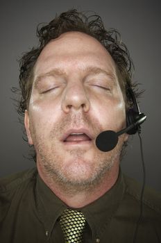 Businessman Sleeps Wearing a Phone Headset Against a Grey Background.
