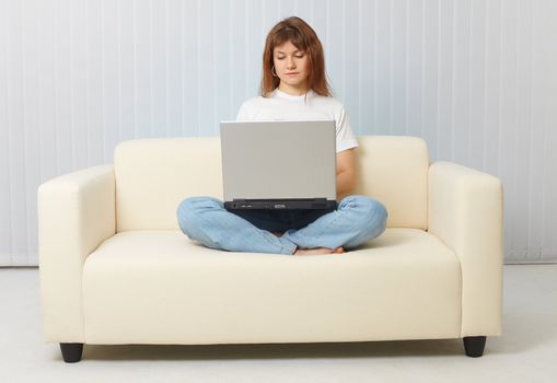 A young woman with a laptop sitting on the couch at home