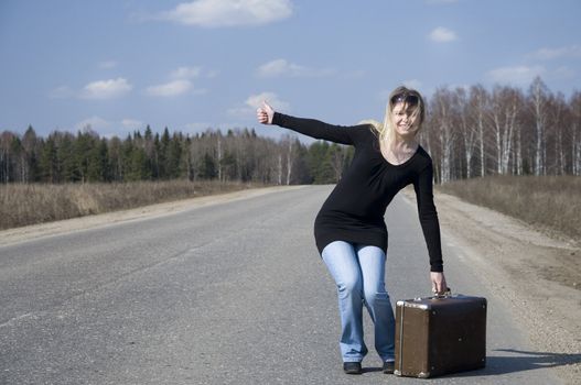 Beautiful country girl hitchhiking on the road with her baggage