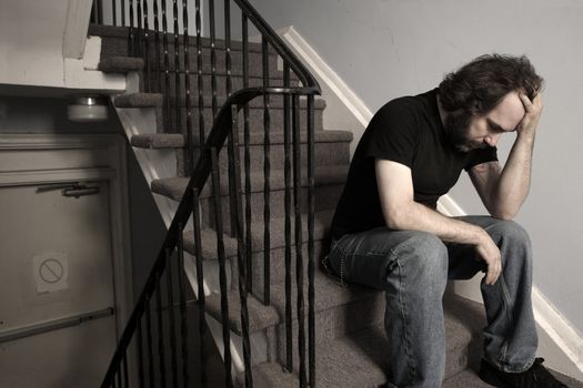 A male adult with overwhelming depression sitting in the stairwell of his apartment building.  Desaturated.
