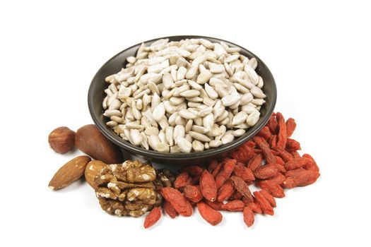 Sunflower seeds in a black bowl with mixed nuts and goji berries on a reflective white background