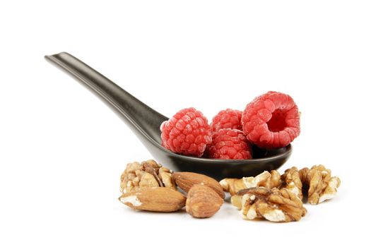 Red ripe frozen raspberries on a small black spoon with mixed nuts on a reflective white background