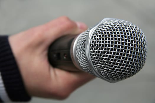 steel microphone in man hand, grey blurred background