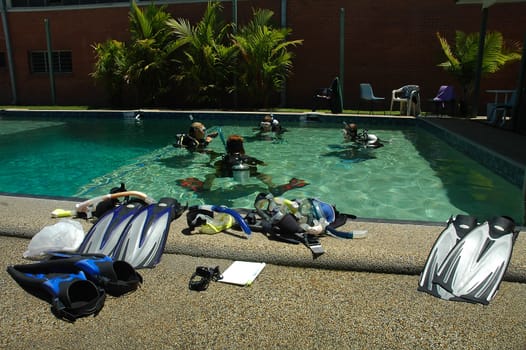 four people practicing diving in small pool, several diving equipment 