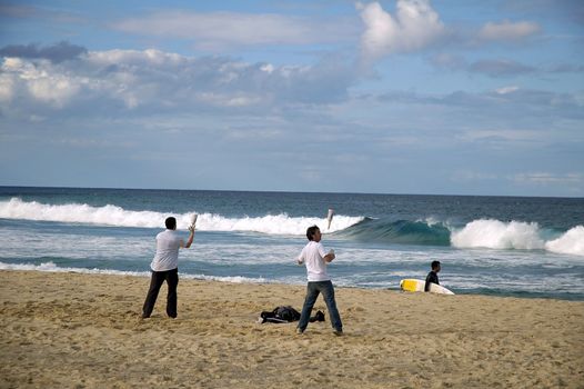 Two young people practising cocktail mixing on a beach,