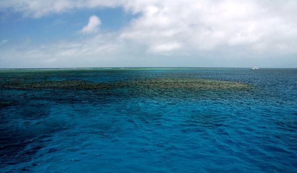 blue calm sea, coral reef, small white boat in background