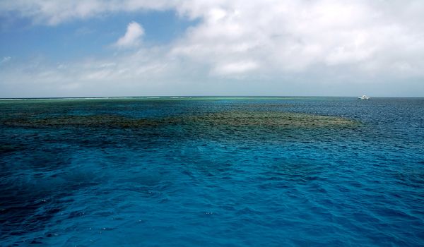 blue calm sea, coral reef, small white boat in background