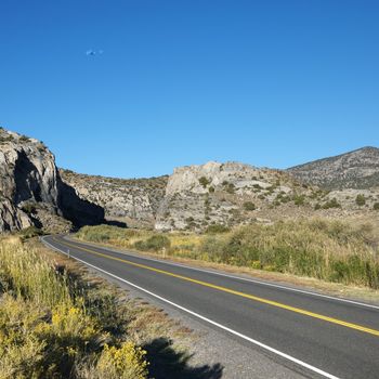 Strip of highway cutting through montain range under clear blue sky.