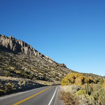 Strip of highway cutting through montain range under clear blue sky.