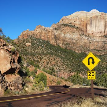 Curve caution sign on two lane road winding through rocky desert cliffs in Zion National Park, Utah.