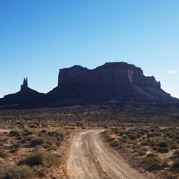 Dirt road headed toward rock formations in desert of Monument Valley, Utah.