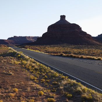Two lane road travelling toward Garden of the Gods rock formation in Monument Valley, Utah.