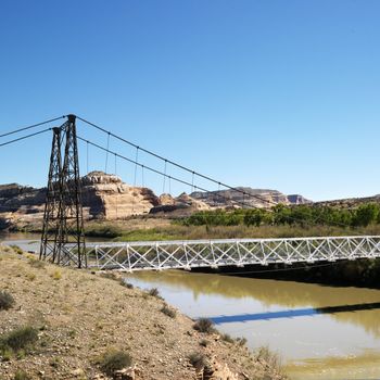 Suspension bridge over river with rock cliffs in Utah.