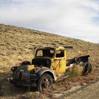 Old yellow dilapidated pickup truck sitting abandoned on hill.