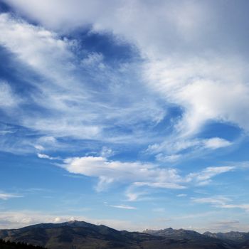 Cloud formations against blue sky with mountain range off in the distance.