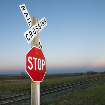 Railroad crossing and stop signs beside railroad tracks in rural setting.