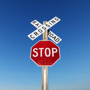 Railroad crossing and stop signs against blue sky.