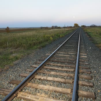 Low angle diminishing view of railroad tracks in rural setting at dusk.