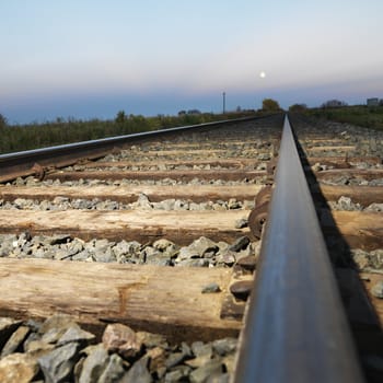 Low angle diminishing view of railroad tracks in rural setting at dusk.