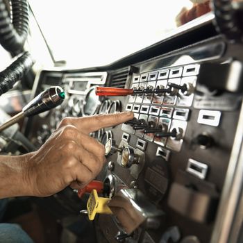 Interior of mid-adult Caucasian male hand pressing switch on dashboard of a tractor trailer.