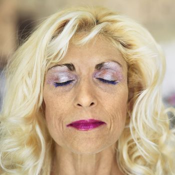 Portrait of tan blonde Caucasion middle-aged woman wearing lots of makeup with eyes closed.