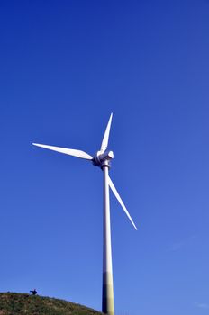 Wind turbine as alternative energy source on green hill with boy pointing to the left and shiny blue sky in the background