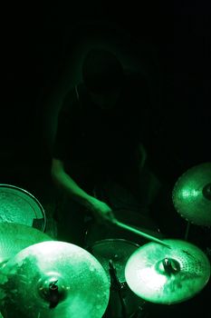 a man in shadow (not visible) is playing on drums, green light