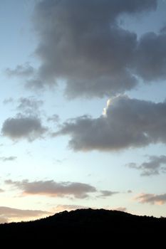 nice cloudy sky and a small forest hill during dusk 