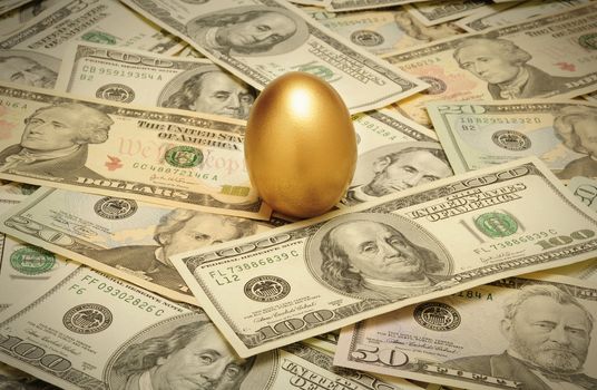 A gold nest egg sitting on a layer of cash of various American banknote denominations