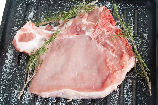 raw pork chop on a griddle with salt and rosemary ready to be cooked