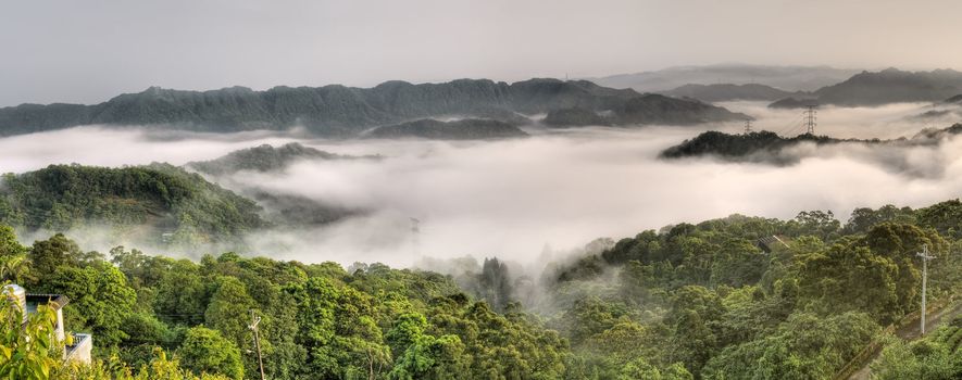 Panoramic landscape of countryside with power tower in mist and clouds.