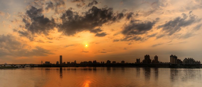 Panoramic cityscape of sunset scenery with building silhouette and river reflection under dramatic sky in dusk in Taipei, Taiwan.