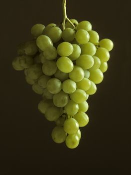 A bunch of green grapes hanging against a dark background