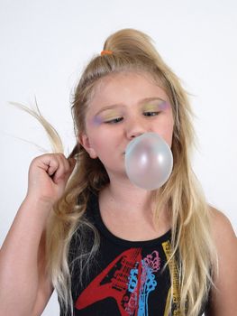 A young blonde girl blowing a bubble and twisting her hair.