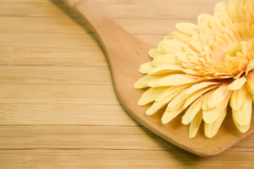 wooden spoon with a yellow flower, on wooden background
