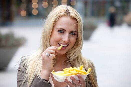 Pretty blond girl eating fries with mayonnaise