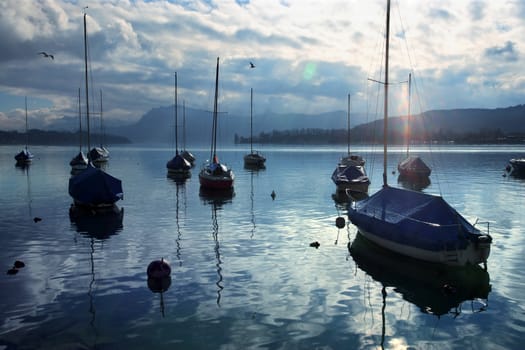 Group of sailboats anchored near the dock just as the sun starts to set.  Lens flare visible.  Taken in Lucerne, Switzerland.
