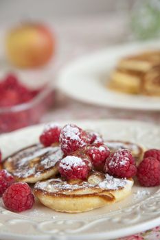 Delicious small blinis with raspberries, icing sugar and honey