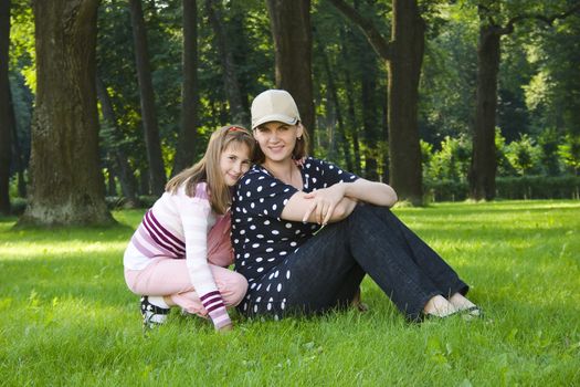 Mother and daughter on lawn in summer's forest.